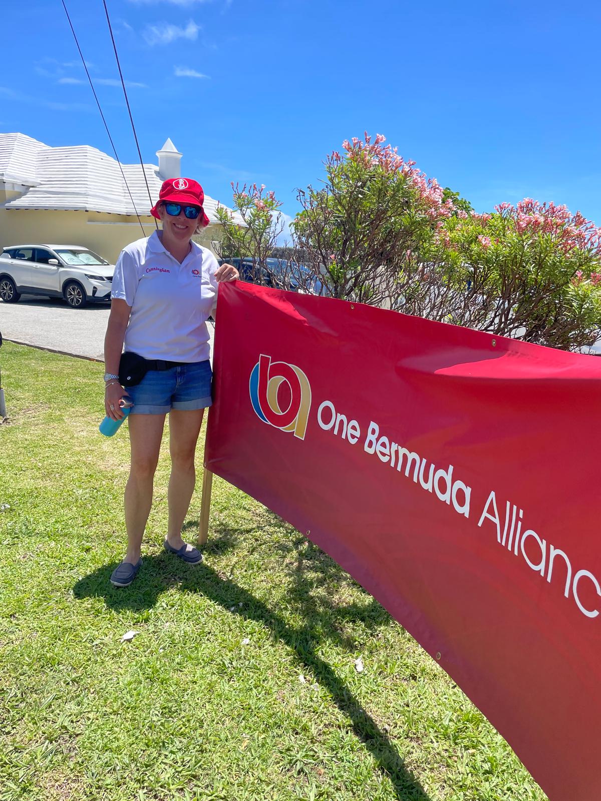 Victoria standing beside a One Bermuda Alliance banner at a sunny outdoor event